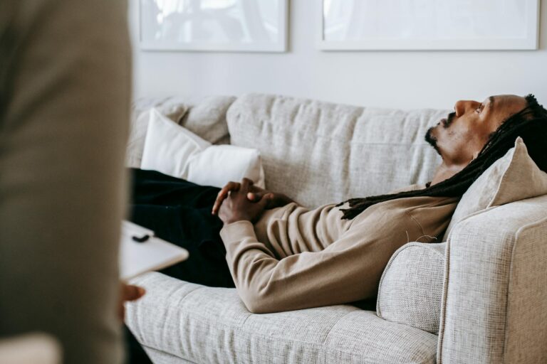 Man in therapy session lying on sofa, conversing with therapist in a relaxed indoor setting.